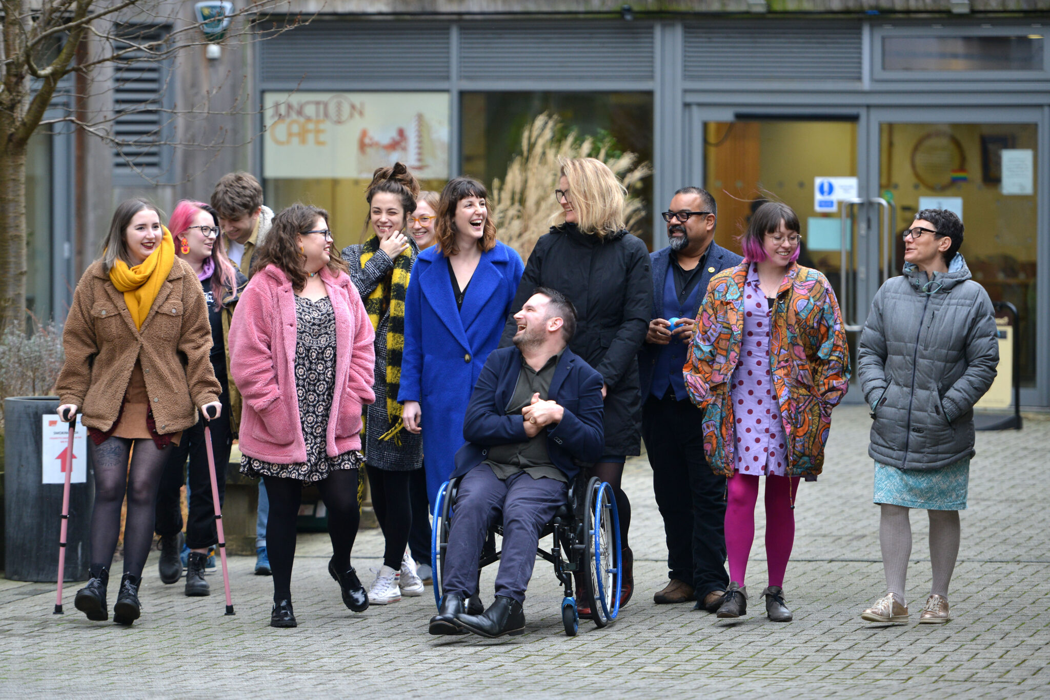 The D&A team outside their office in Brighton. They are walking or wheeling towards the camera, but are looking at each other, chatting and smiling as they go. They are a diverse mix of ages, races, disabilities and genders.