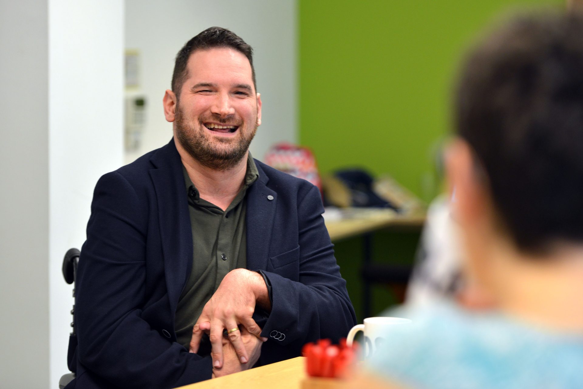 A man smiles at another person off screen in a one-to-one. 