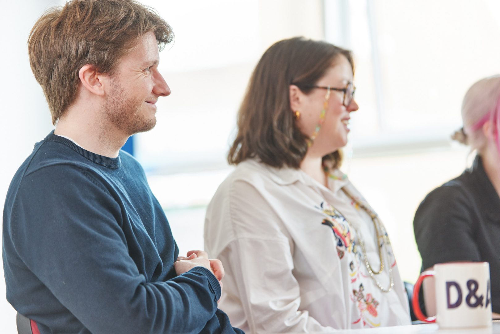 Two people are sat next to each other, facing the same direction. Their smiles show they're listening intently to a speaker.