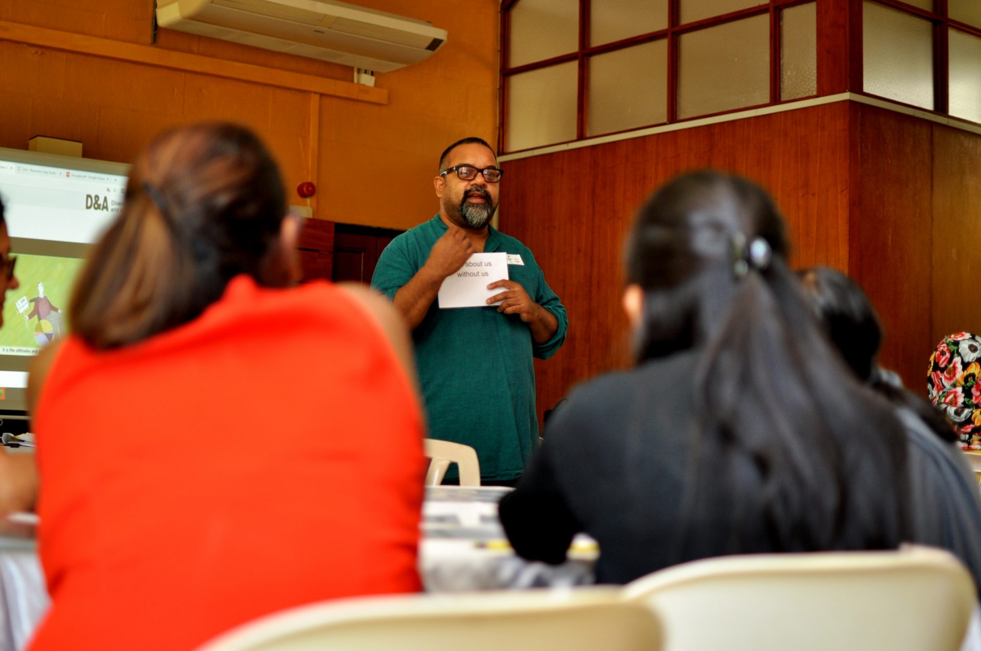 Atif, a brown man with dark hair and a beard, is standing at the front of a classroom and speaking to a group of people.