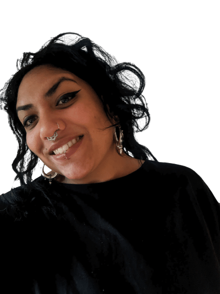 A person of Indian origin with Gujarati roots with thick, dark curly hair wearing silver earrings and dressed in black. She has a septum,nose and lip piercing.
