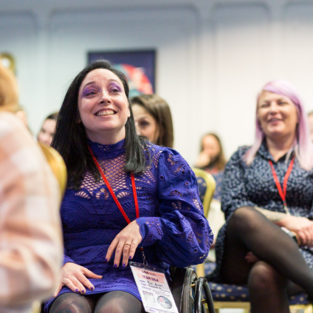 A wheelchair user wearing an all purple outfit at a conference.