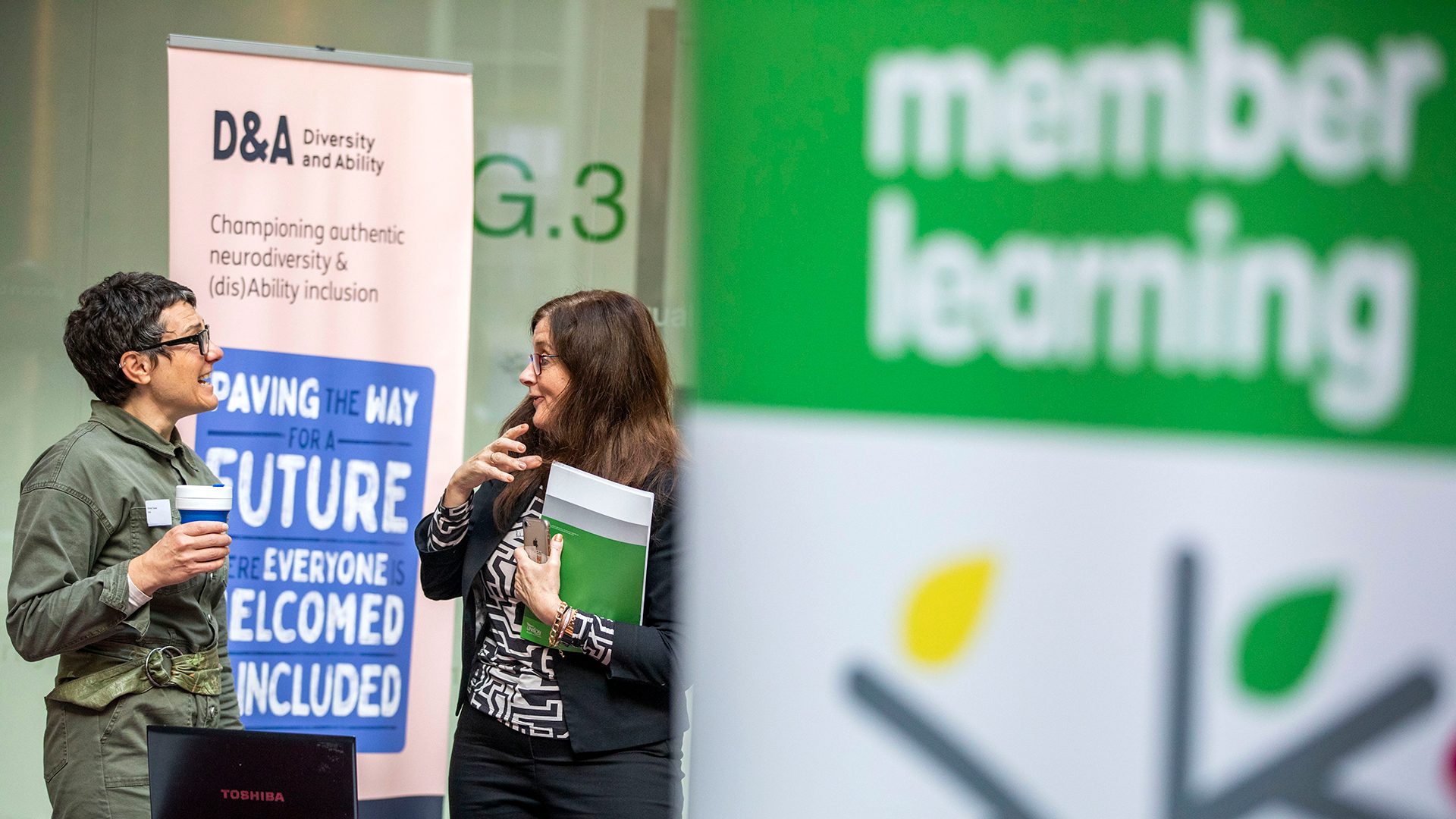 Two people standing in front of the Diversity and Ability banner, talking to each other animatedlty.