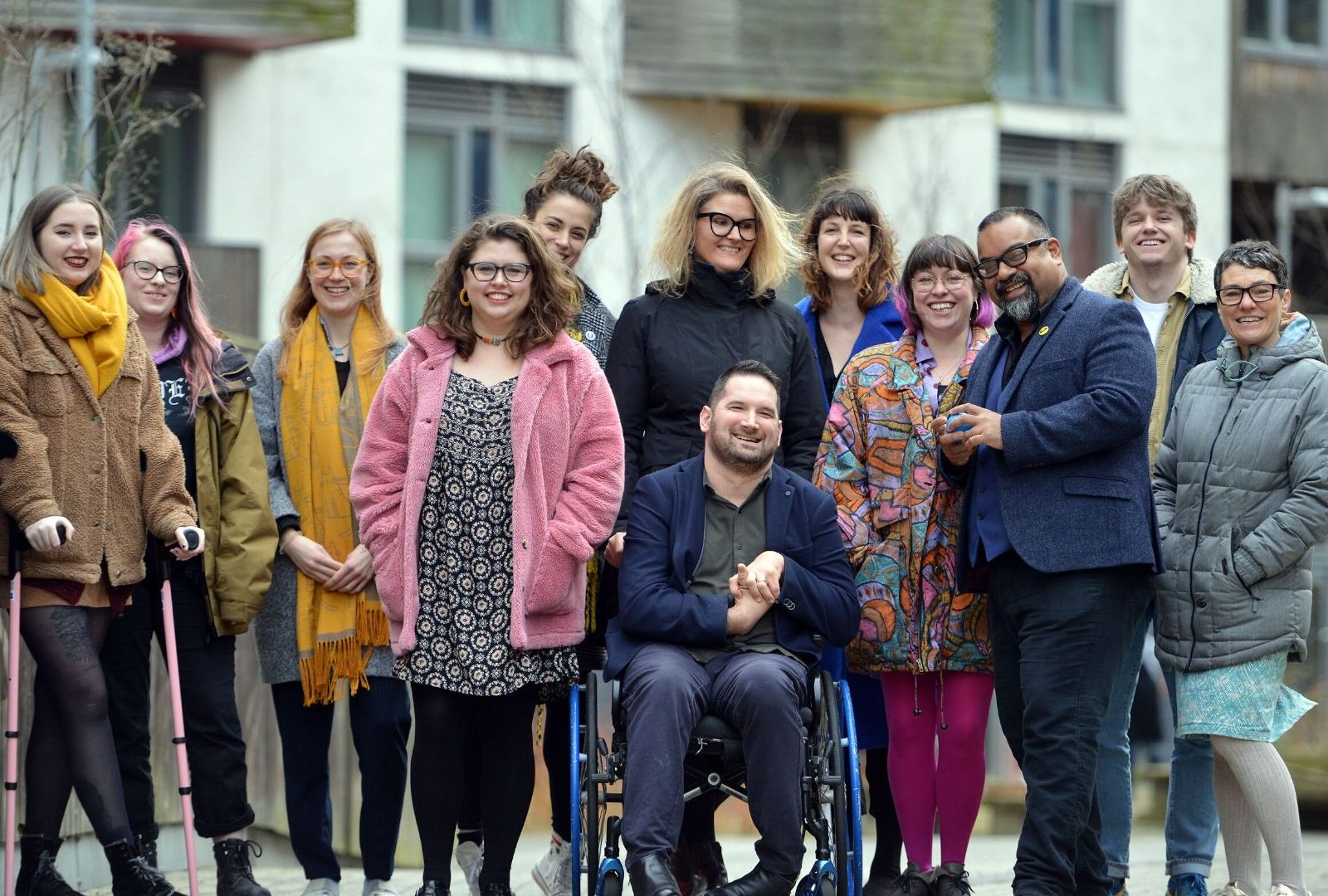 The D&A team outside their office in Brighton. They are moving towards the camera, but are looking at each other, chatting and smiling as they go. They are a diverse mix of ages, races, disabilities and genders.